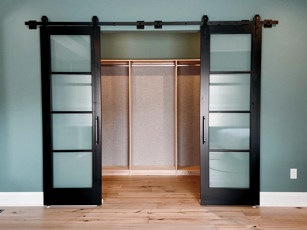 Black metal sliding closet doors with frosted divided glass and exposed overhead hardware.